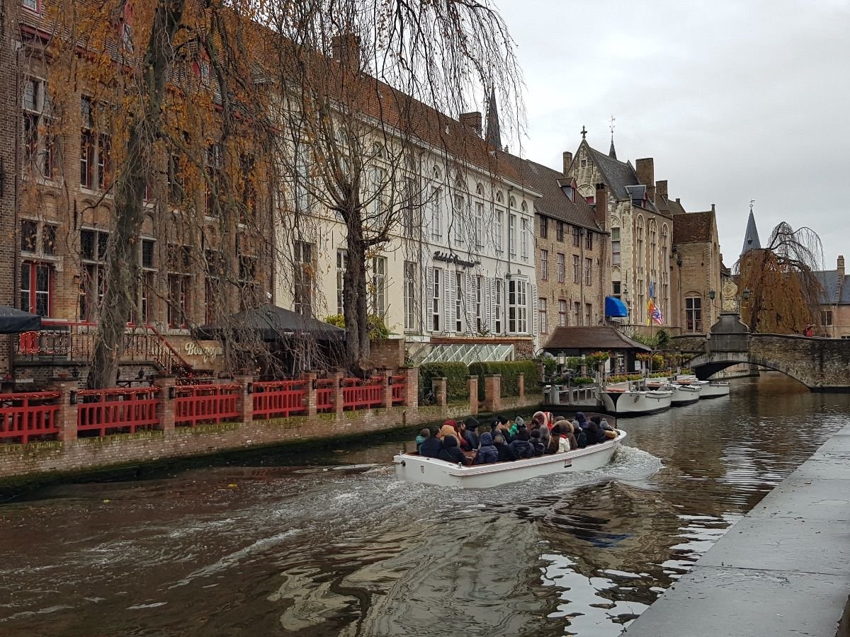 Barco turístico navegando por los canales de Brujas con casas medievales alrededor